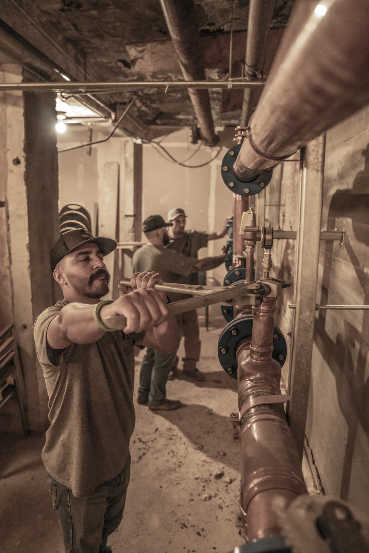 True Tex plumbers wrenching flanged copper main lines in a commercial basement
