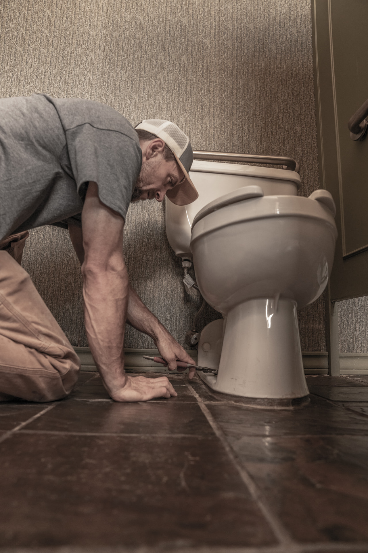 Plumber tightening the base bolts on a toilet during a repair