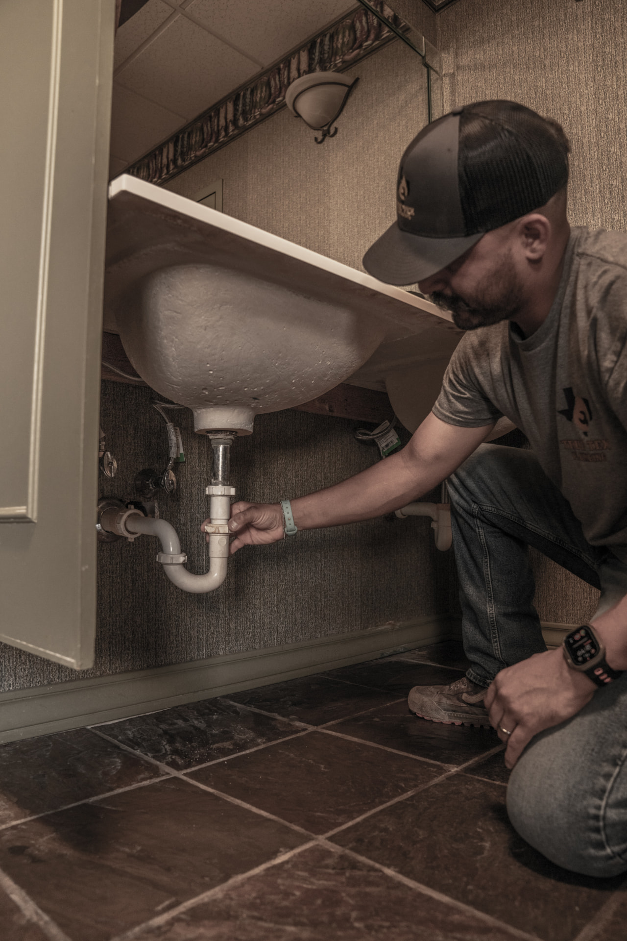 True Tex plumber repairing a leaking P-trap under a bathroom sink